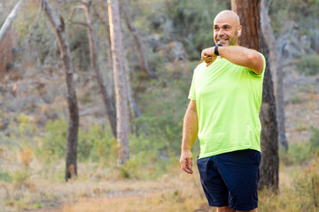 Sporty man talking on the phone through smart watch, in the forest