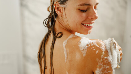 A woman enjoys a refreshing shower, applying shampoo and smiling, reflecting happiness and wellness