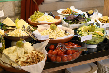 A wide selection of fresh cheeses, olives, tomatoes, cucumbers, nuts, and fruits displayed at the self-service breakfast buffet in a hotel restaurant