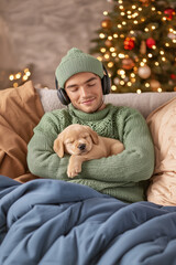 puppy dog sleeps in the arms of his owner who is listening to music with headphones, christmas decoration, face of happiness, peace, tranquility, vertical,
