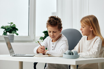 Happy children studying together at home using laptops and tablets for online education The brother and sister are sitting at a table in their cozy living room, fully concentrated on their elearning