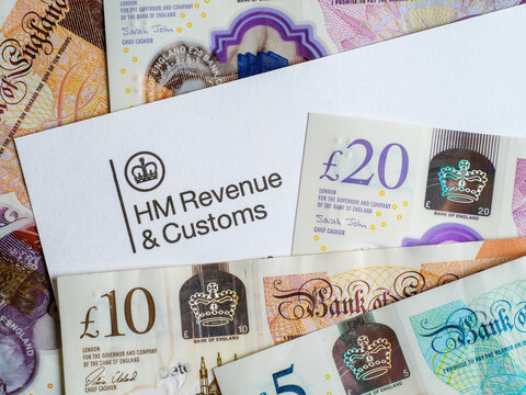 Close up of income tax letter from HMRC or Inland Revenue among a pile of British pound notes in cash, UK