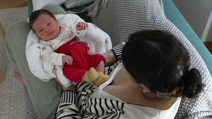 Baby gazing intently while resting in mother's arms, wrapped in a soft blanket, wearing vibrant red...