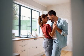 Romantic couple dancing in kitchen at home.