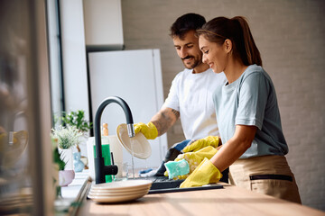 Happy couple washing dishes together in kitchen.