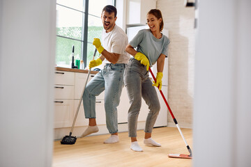 Carefree couple singing and dancing while cleaning their home.