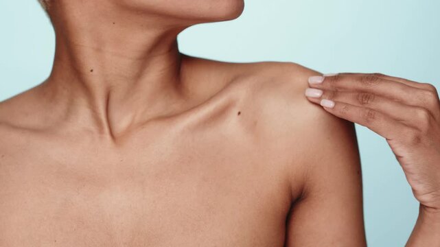 Close-up of a unrecognizable woman's upper body, hand gracefully touching chest on a blue background, portraying concepts of beauty and body care.