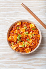 Mapo tofu, a popular Chinese Sichuan dish, served in a bowl and garnished with green onion, on white wooden background