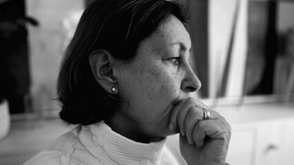 Black and white portrait of an elderly woman deep in thought, hand on her chin, emphasizing the...