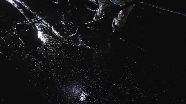 A worker in protective wear stands in crude oil and cleans it out with a shovel. Cleaning oil tanks from oil residues