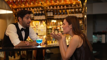 Sitting in smiling beautiful woman guest lively taking with smart bartender while drinking mixed...