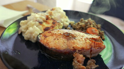 Grilled salmon steak served with creamy mashed potatoes and a side of sautéed lentils with carrots, showcasing a balanced and nutritious meal presentation