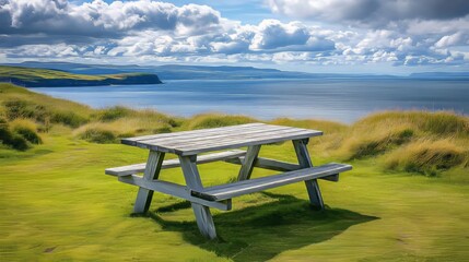 Obraz premium Picturesque Picnic Table Overlooking a Serene Blue Water Bay Under a Cloudy Sky