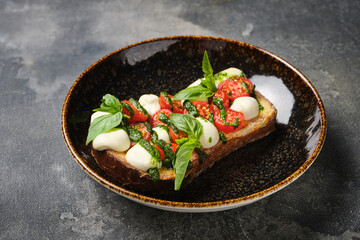 close-up view of a delicious caprese bruschetta with ripe tomatoes, fresh basil, and creamy mozzarella on a dark, textured plate.