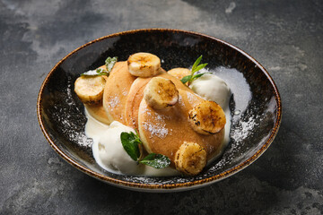 delicious serving of soft pancakes topped with banana slices and a scoop of vanilla ice cream, presented in a textured bowl.