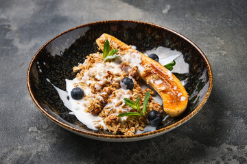 delicious serving of grilled banana topped with crunchy granola, fresh blueberries, and a drizzle of creamy yogurt, beautifully presented in a textured bowl.