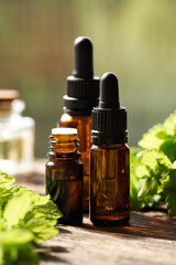 Three brown bottles of aromatherapy essential oil with fresh melissa leaves