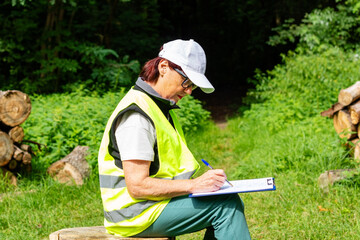 Forestry inspector records logging data. Mature female eco engineer with tablet checks felled trees. Ecologist.