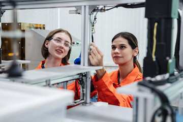 Student engineer assembles a robotic arm in a technology workshop. Engineer holds a robot controller and inspects the robotic arm's welding hardware.