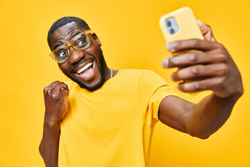 Young man taking a selfie, wearing a yellow shirt and glasses, expressing happiness and excitement,...