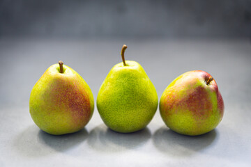 Three ripe pears with green and red skin, arranged in a row on a neutral background