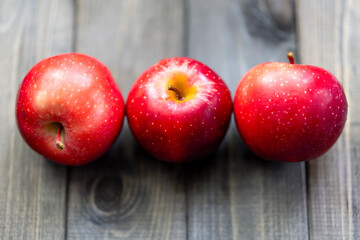 Three bright red apples arranged in a row on a wooden surface