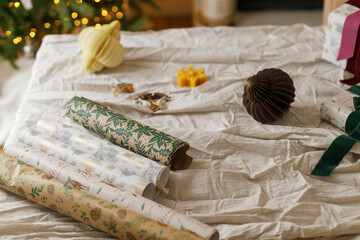 Wrapping stylish christmas gift, winter holidays preparation. Modern wrapping paper, ribbons and stylish ornaments on table with linen cloth. Details of festive decorations