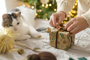 Wrapping stylish christmas gift, winter holidays preparation. Hands in cozy sweater decorating gift...