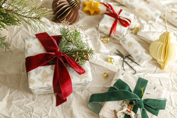 Stylish christmas gift box and modern ornaments on linen cloth. Merry Christmas and Happy Holidays. Wrapped Christmas presents with red and green ribbons, fir branches and vintage toy