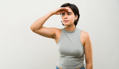 Studio portrait of a young latin woman with short hair shielding her eyes from the sun while looking into the distance