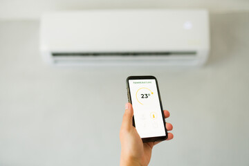 Man using a mobile app to adjust the air conditioner temperature in a bedroom while holding a...