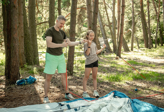 Father And Daughter Setting Up A Tent While Camping In The Forest