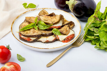 Eggplant dish, on a plate on a light background. Italian cuisine, eggplants with tomato sauce and mozzarella. Horizontal.