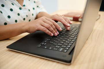 Close-up of hands typing on laptop keyboard at wooden desk, office or home workspace setting