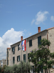 Croatian flag on the side of a stone building with a blue sky and trees, building, architecture, sky, house, factory, chimney, industry, old, tower, industrial, plant, window, brick, clouds, station, 