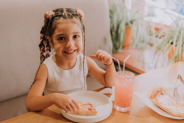 little girl eats pizza and drinks a cocktail in a pizzeria