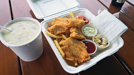 Seafood - a white takeout container with fish and chips - breaded fried fish and French fries,...