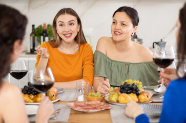 Girlfriends chatting and drinking wine at home party table in kitchen