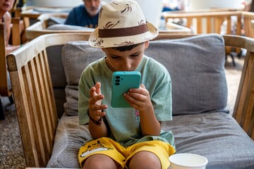 niño muy joven con sombrero de paja jugando con un movil azul
