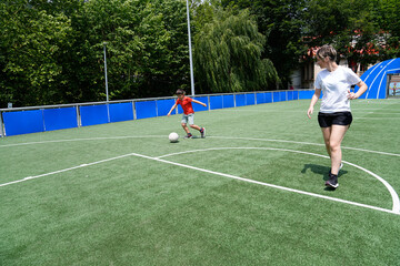 Fototapeta premium Mother and son playing soccer on a bright green field, kicking the ball to each other.