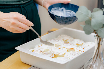 A young girl spreads cream on the Cinnabons in a baking dish on the table.
