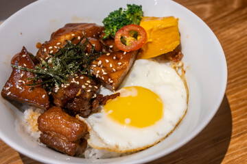 A mouthwatering Asian dish featuring sweet and savory pork belly, a sunny-side-up egg, and fresh vegetables served over rice in Tainan, Taiwan. Perfect for lunch or dinner.