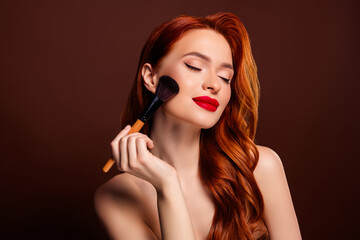 Fototapeta premium Photo of stunning rich lady model applying foundation highlighter isolated on brown color background
