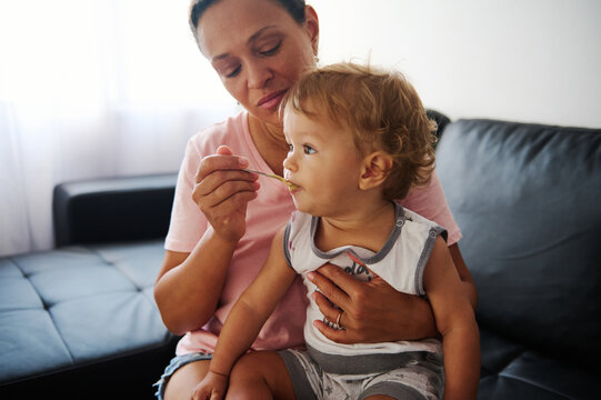 Mother feeding toddler at home, capturing a loving and nurturing moment on a comfortable couch in a cozy living room setting