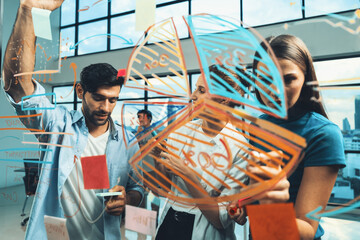 Skilled project manager pointing at glass wall while coworker thinking about plan. Diverse business team working together, brainstorming marketing idea or business plan. Creative start up. Tracery.