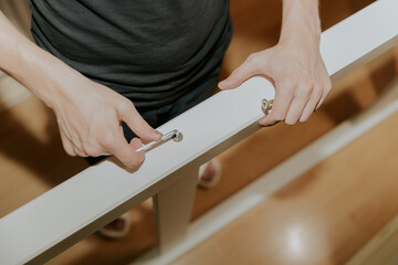 A young man hand screws a screw into a hole in the side of a bunk bed.