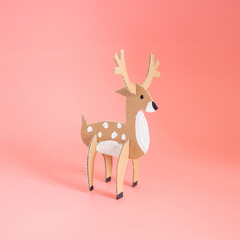 Three dimensional paper craft model of a brown deer with white spots and antlers on a plain pink background, profile view facing right, ideal for DIY animal model and craft enthusiasts.