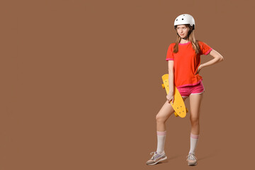 Beautiful young woman in helmet with skateboard on brown background