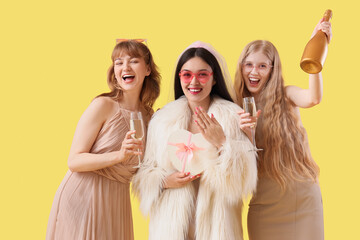 Young Asian woman with gift and her bridesmaids on yellow background. Hen Party