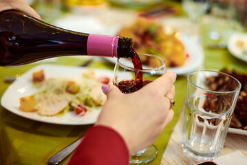 hand holds a glass into which red wine is pouring from a bottle